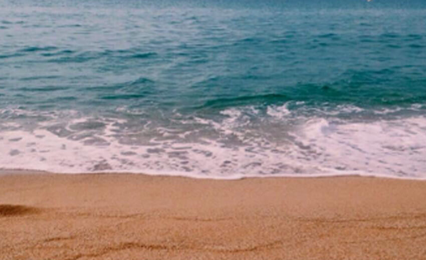 Clear turquoise water meeting wet sand on an empty Barcelona beach