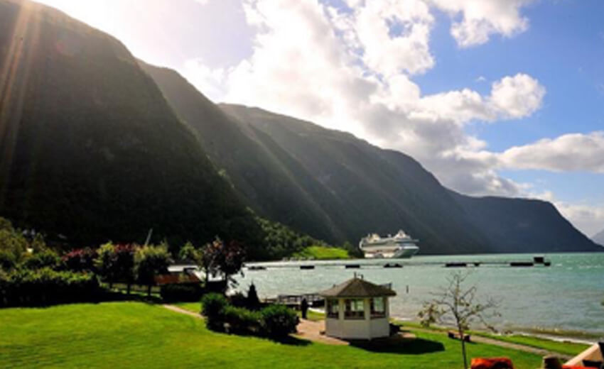 A ship moored in a Norwegian fjord below steep green cliffs