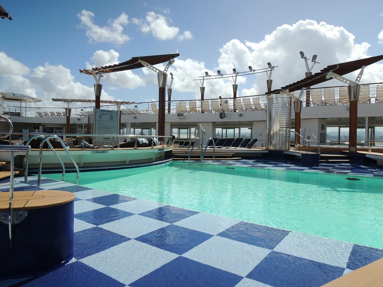 A ship's deck pool tiled in blue and white, shade sails overhead