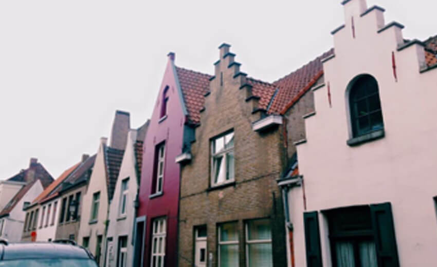 A row of stepped gable houses in pink, grey and cream against a pale sky in Bruges