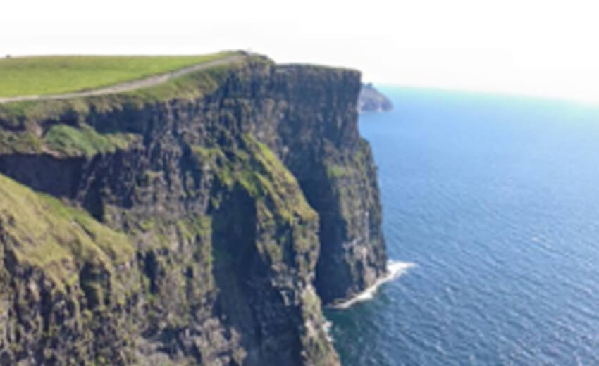 The Cliffs of Moher dropping straight into the Atlantic, green grass along the clifftop