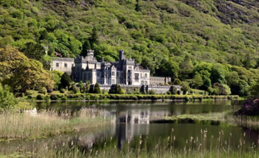 Kylemore Abbey on the lakeshore in Connemara, wooded hillside rising behind it