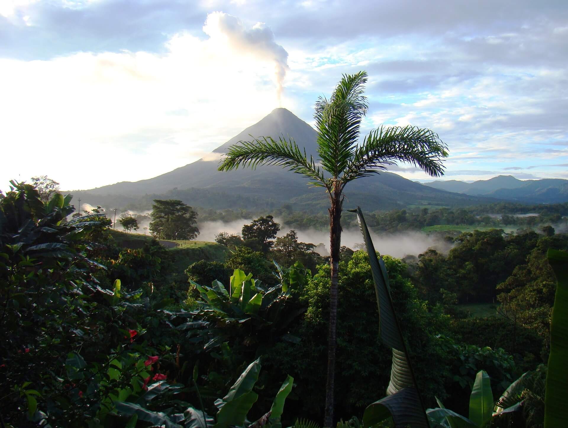 Arenal volcano with cloud sitting on the summit and mist lying over banana palms below
