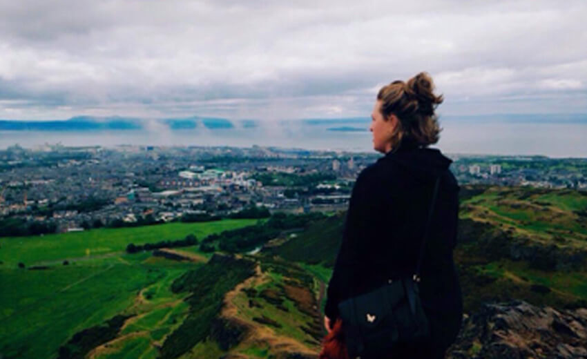 A walker on Arthur's Seat looking down over Edinburgh and the green slopes below
