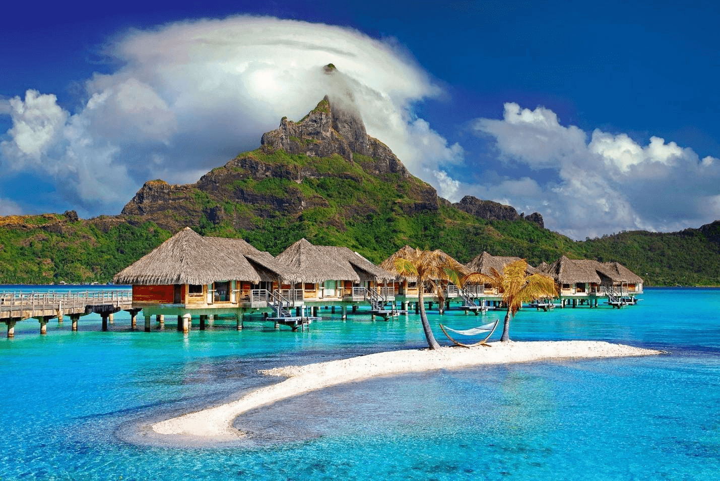 Overwater bungalows on stilts in a turquoise lagoon below Mount Otemanu, Bora Bora