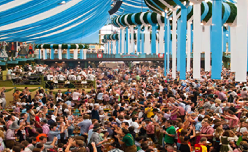 A packed Oktoberfest beer tent in Munich, long tables under striped canopies