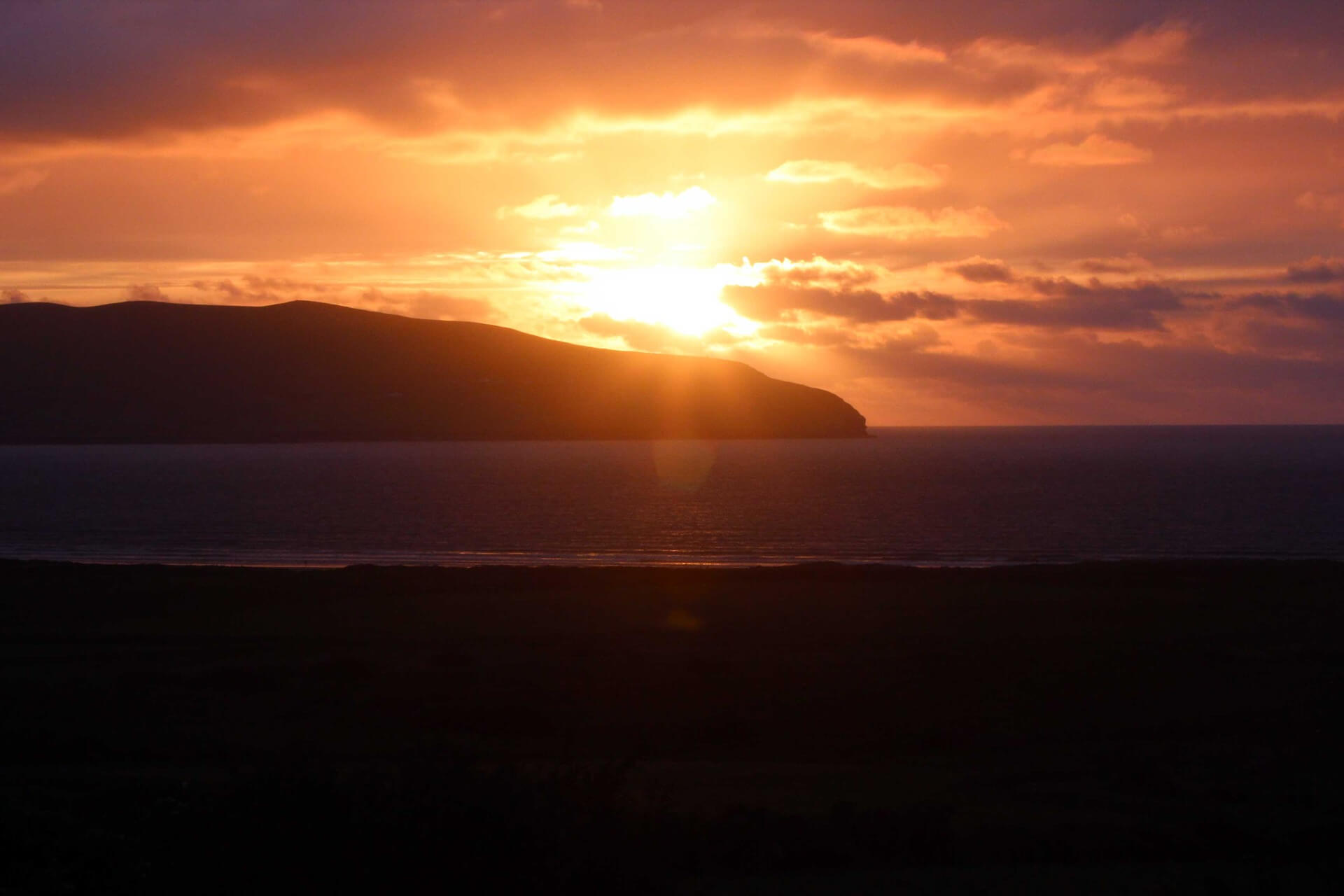 The sun dropping behind a headland across a bay on the west coast of Ireland