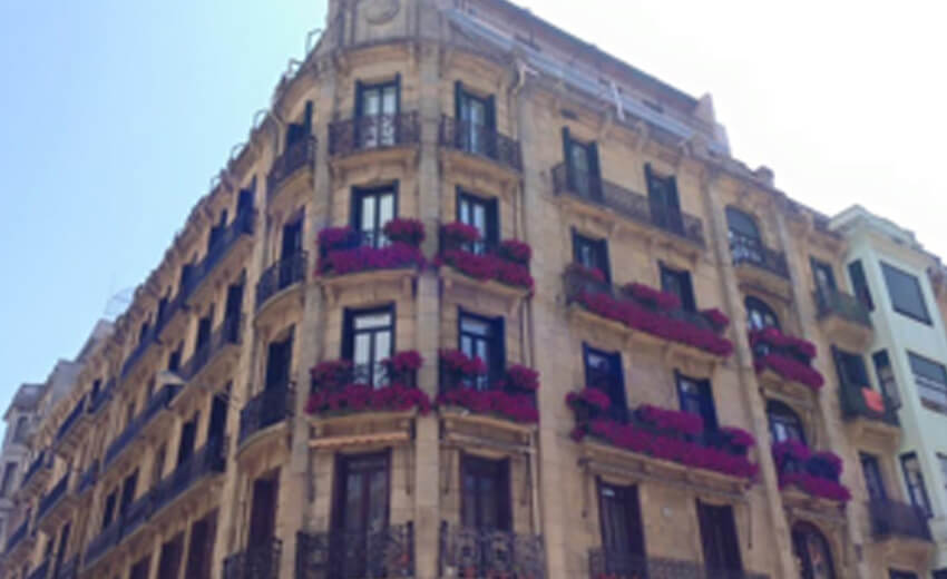 A curved Belle Epoque apartment building in San Sebastian with red awnings and iron balconies