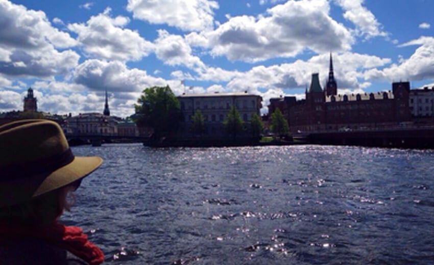 A passenger in a straw hat on a boat, the Stockholm waterfront and spires across the water