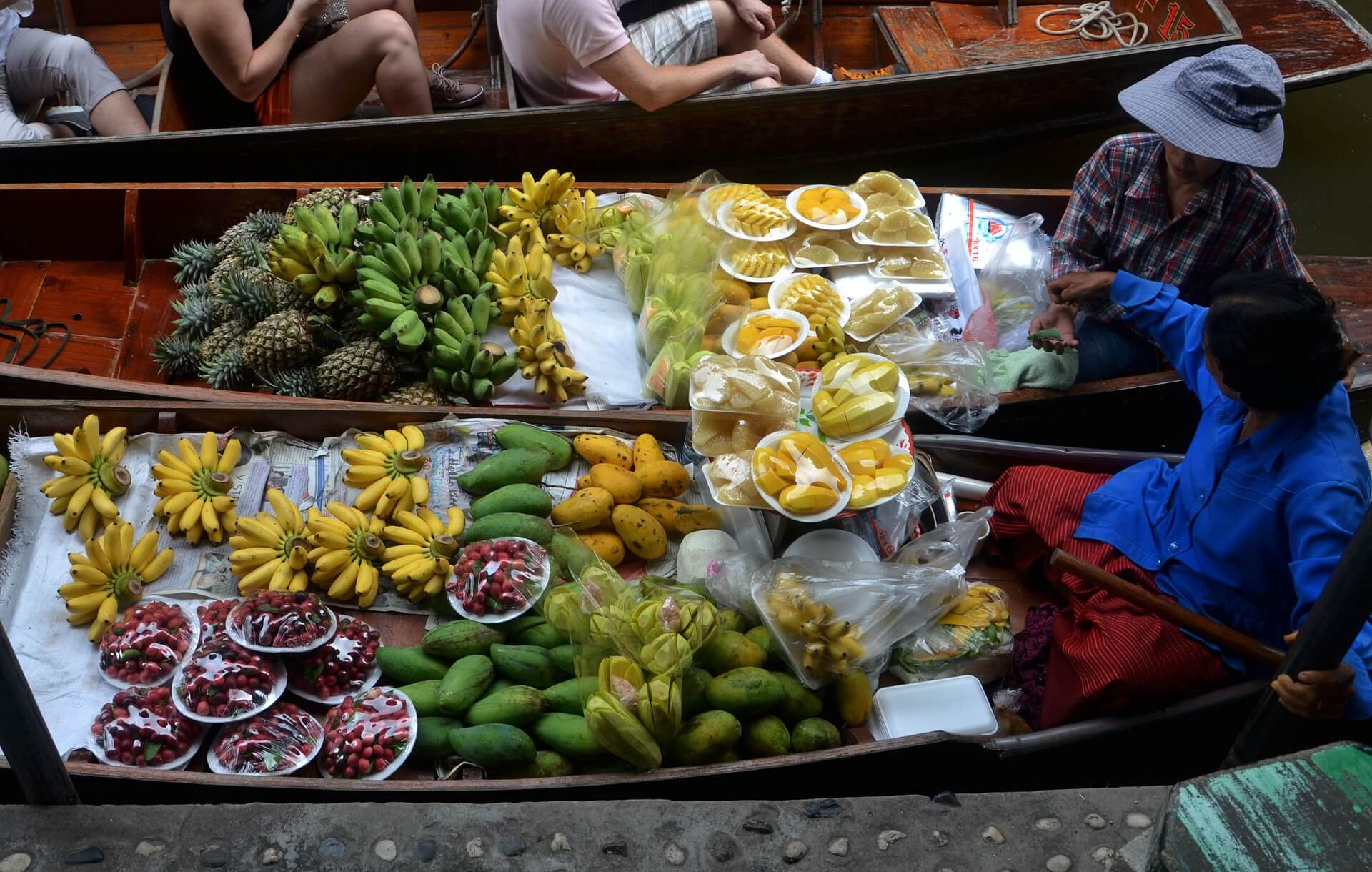 Vendors at a Thai floating market, long-tail boats loaded with bananas, pineapples and mangoes