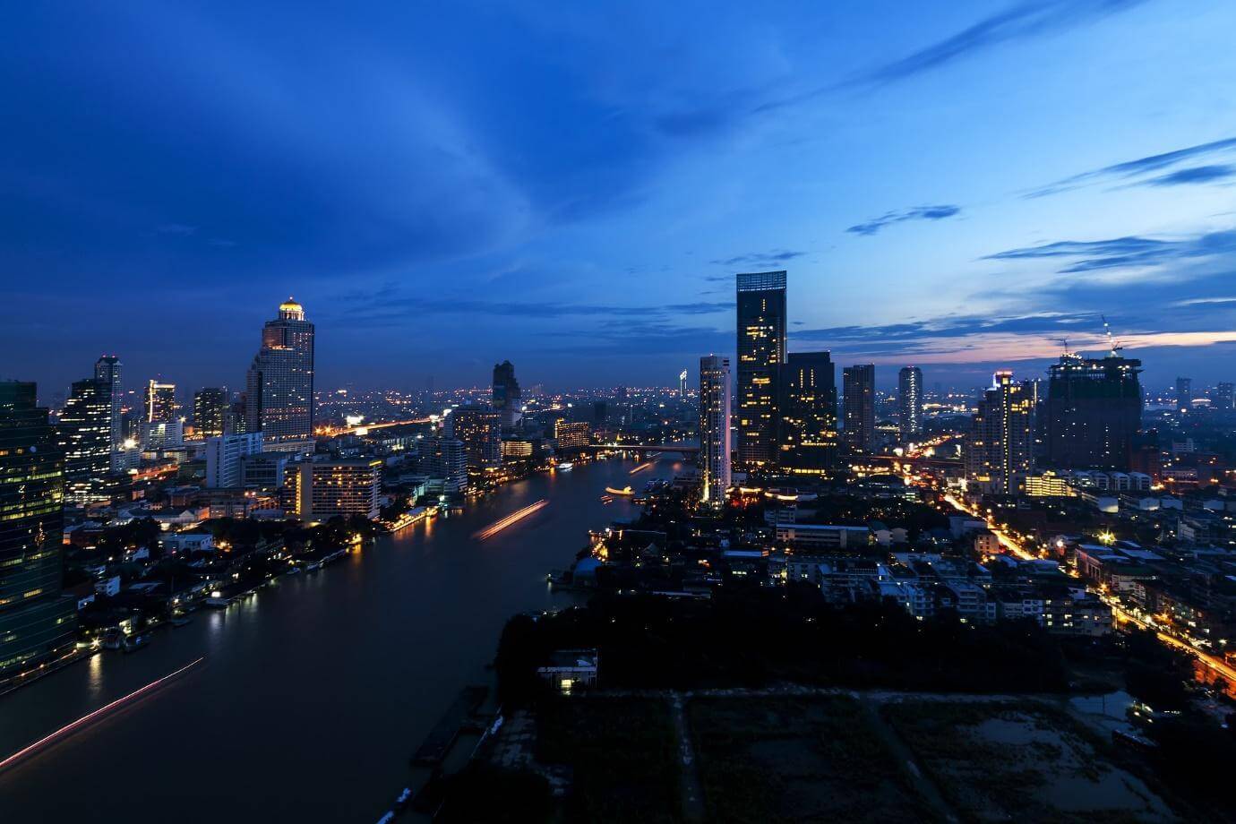Bangkok at dusk, the Chao Phraya river curving between lit towers