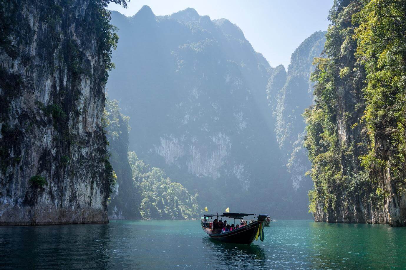 A long-tail boat crossing green water between limestone karsts in southern Thailand